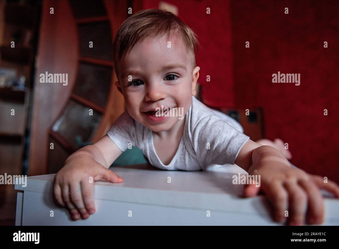 Portrait of toddler in gray bodysuit lying on white chest of drawers in