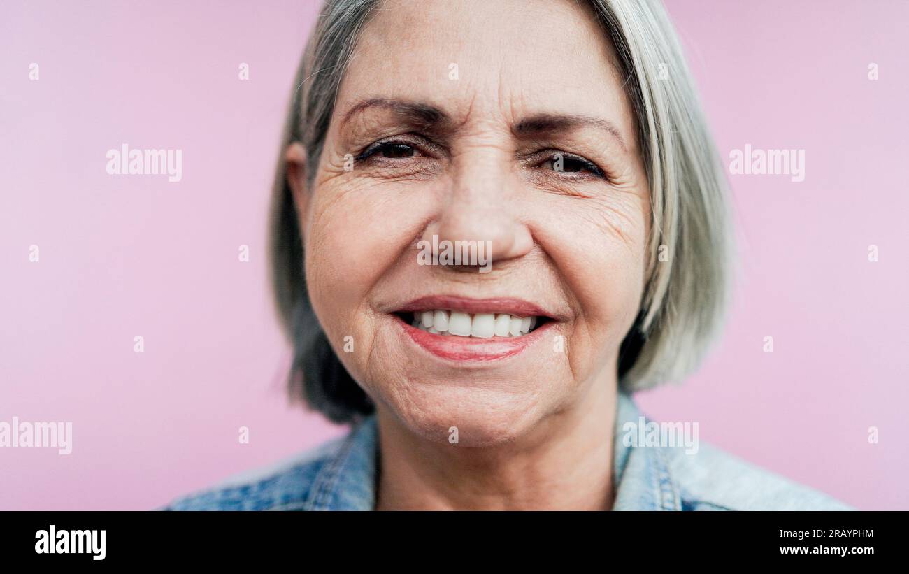 Happy senior Latin woman having fun smiling on camera with pink ...