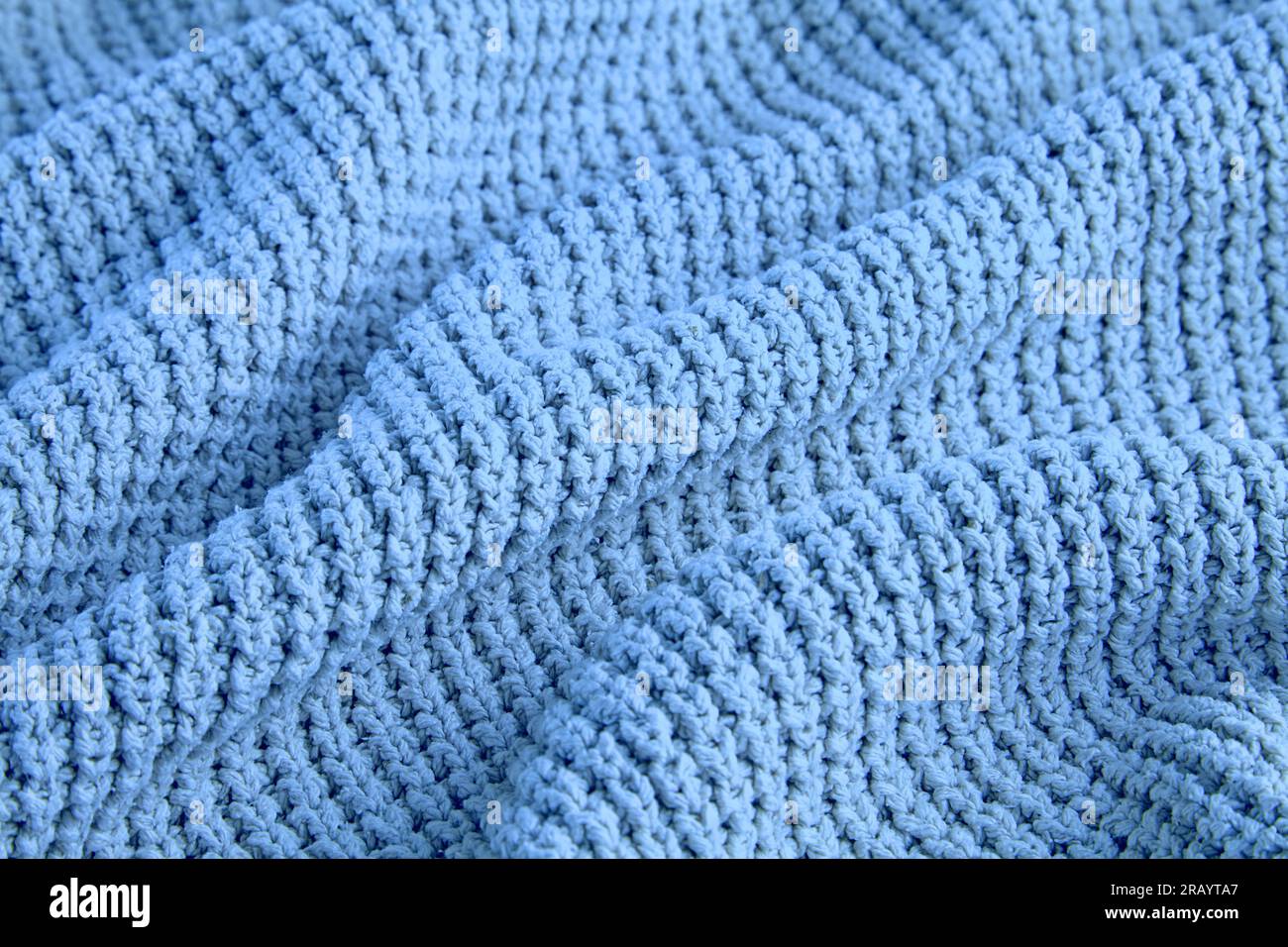 blue knitted clothes of coarse knit with folds and shadows as a background for design. Stock Photo