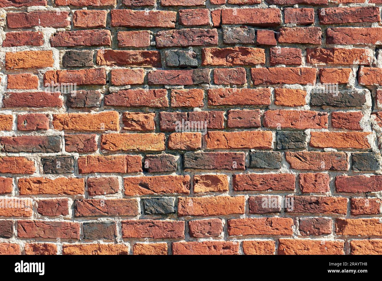 Wall of antique handmade baked bricks with cracks and holes. Background of medieval brickwork for design Stock Photo