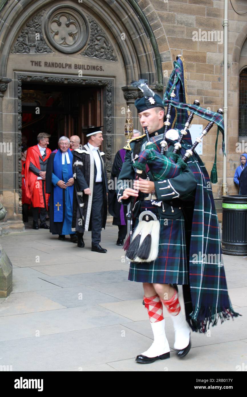 Scottish piper leaving Glasgow university building followed by university staff in gowns on graduation day Stock Photo