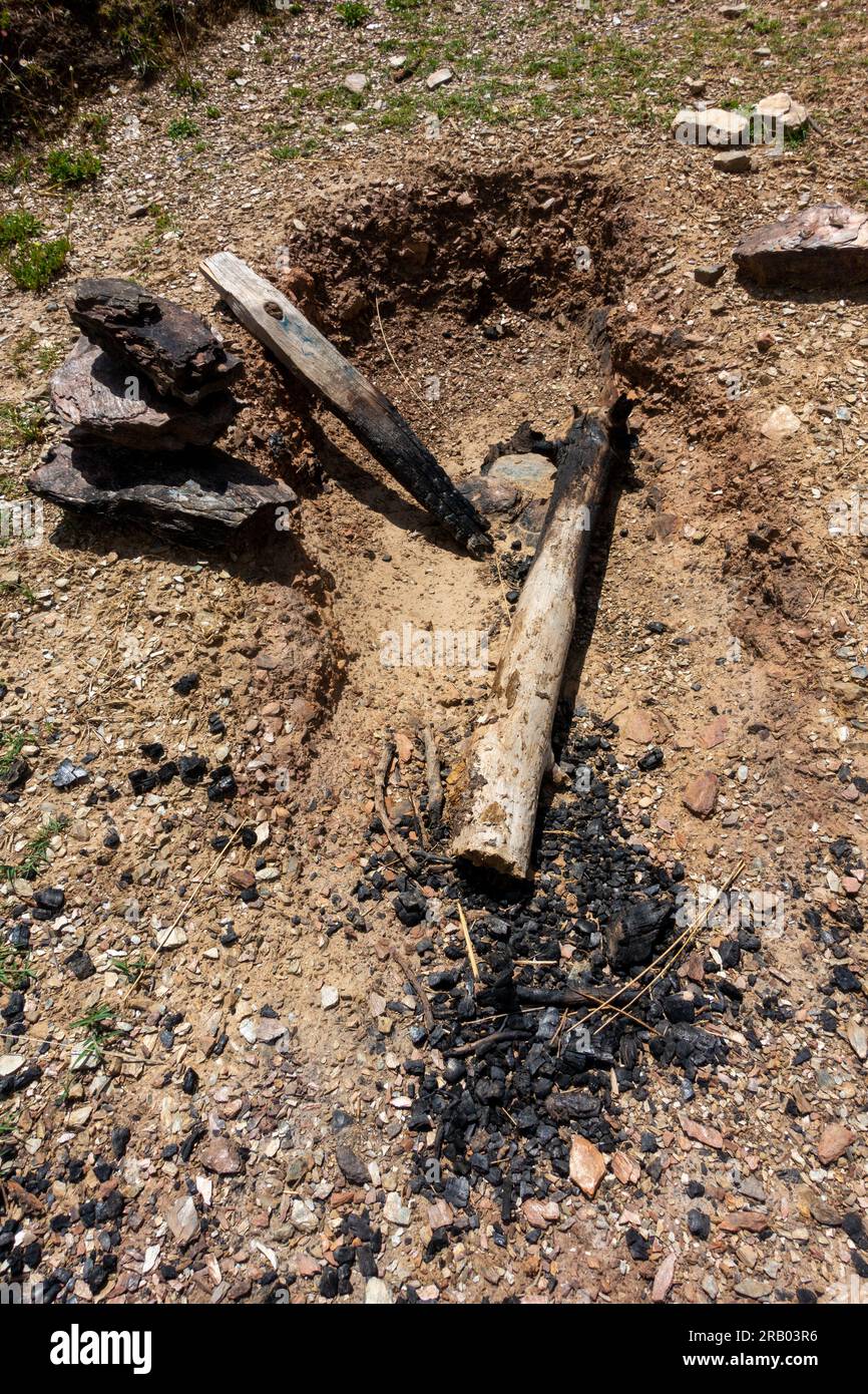 An outdoor dug up burned out fire pit into the earth with residual firewood logs and ashes