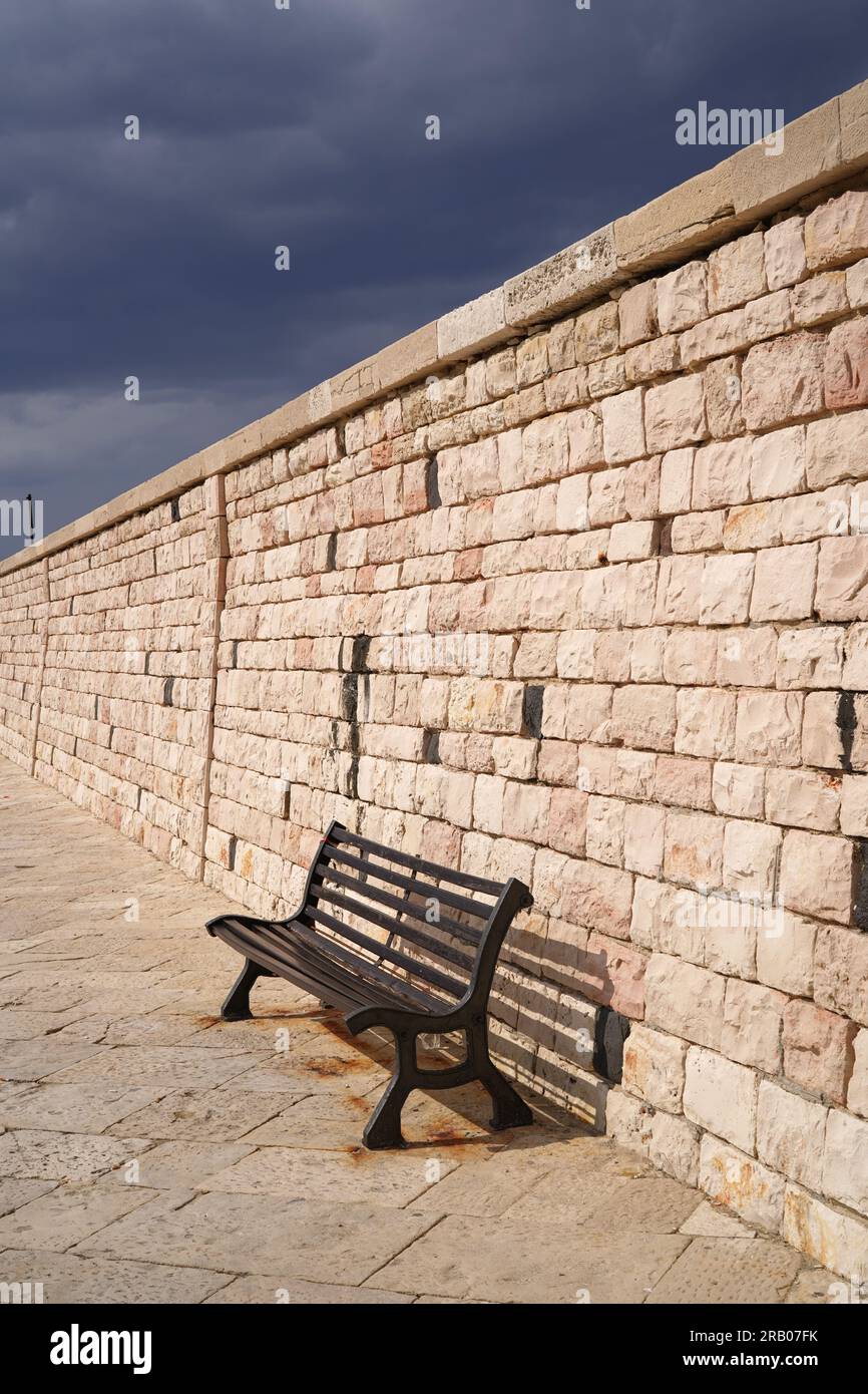 bench next to stone breakwater at the port Stock Photo