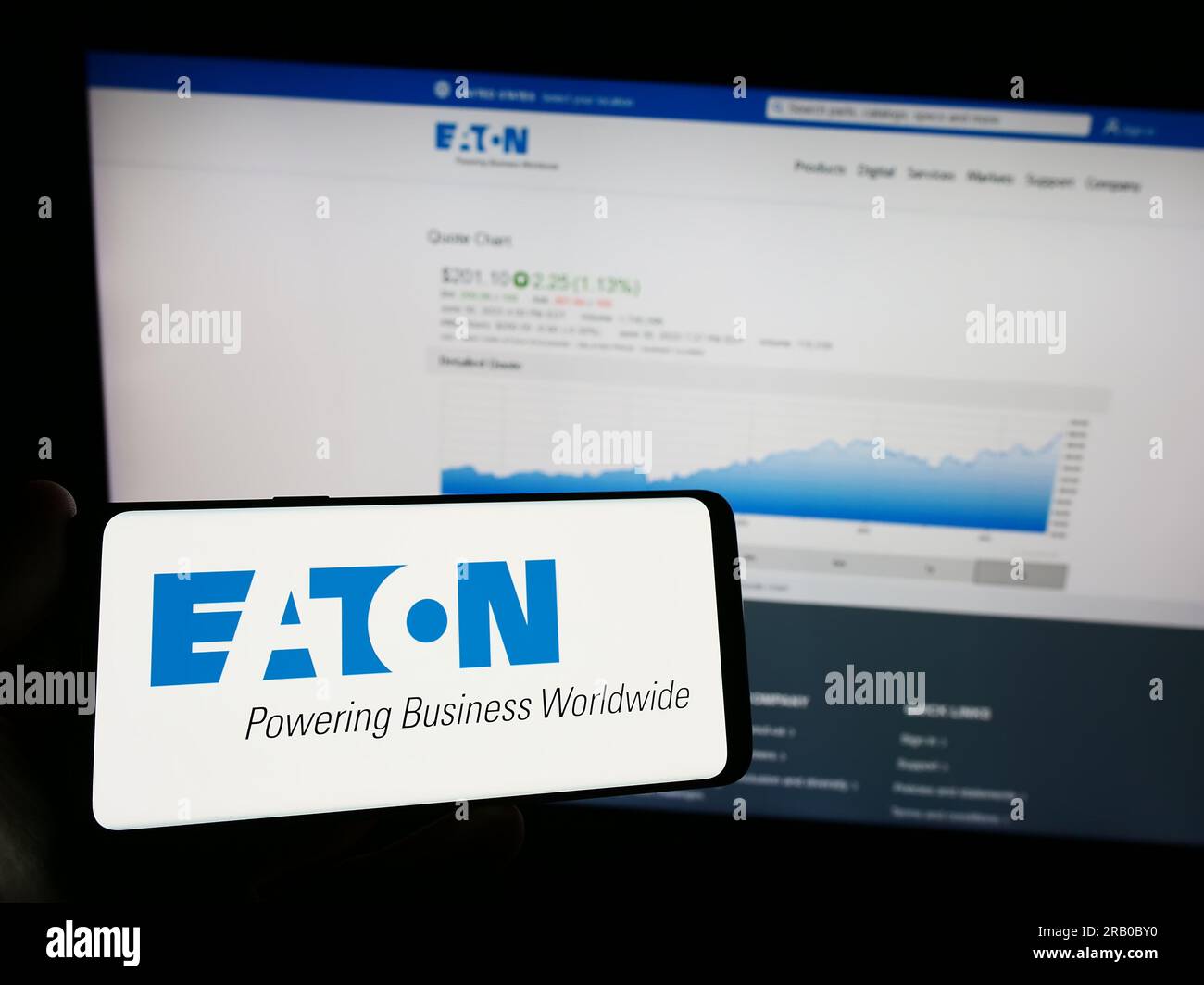 Person holding mobile phone with logo of power management company Eaton Corporation plc on screen in front of web page. Focus on phone display. Stock Photo
