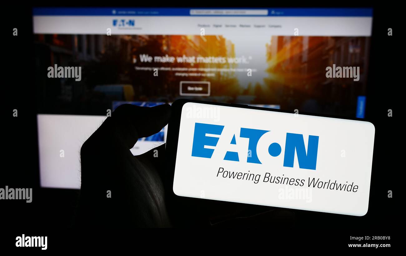 Person holding smartphone with logo of power management company Eaton Corporation plc on screen in front of website. Focus on phone display. Stock Photo