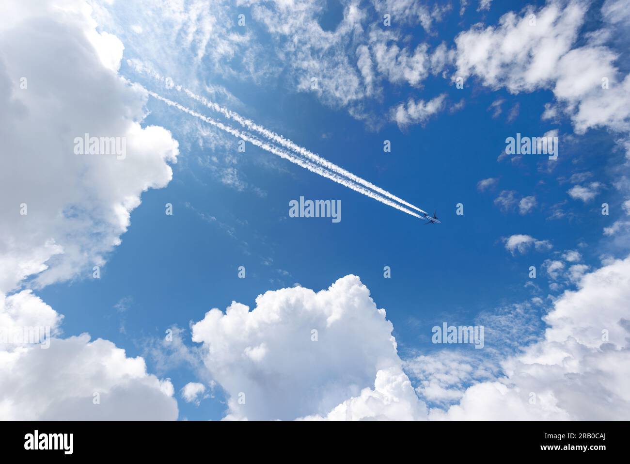 Airliner with contrails flying in a clear blue sky with beautiful cumulus clouds or cumulonimbus. Photography, Full frame. Stock Photo