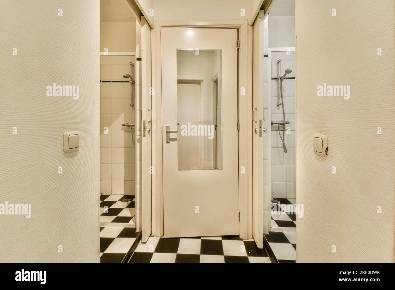 a bathroom with black and white checkered tiles on the floor, and an open door leading to a walk - in shower Stock Photo
