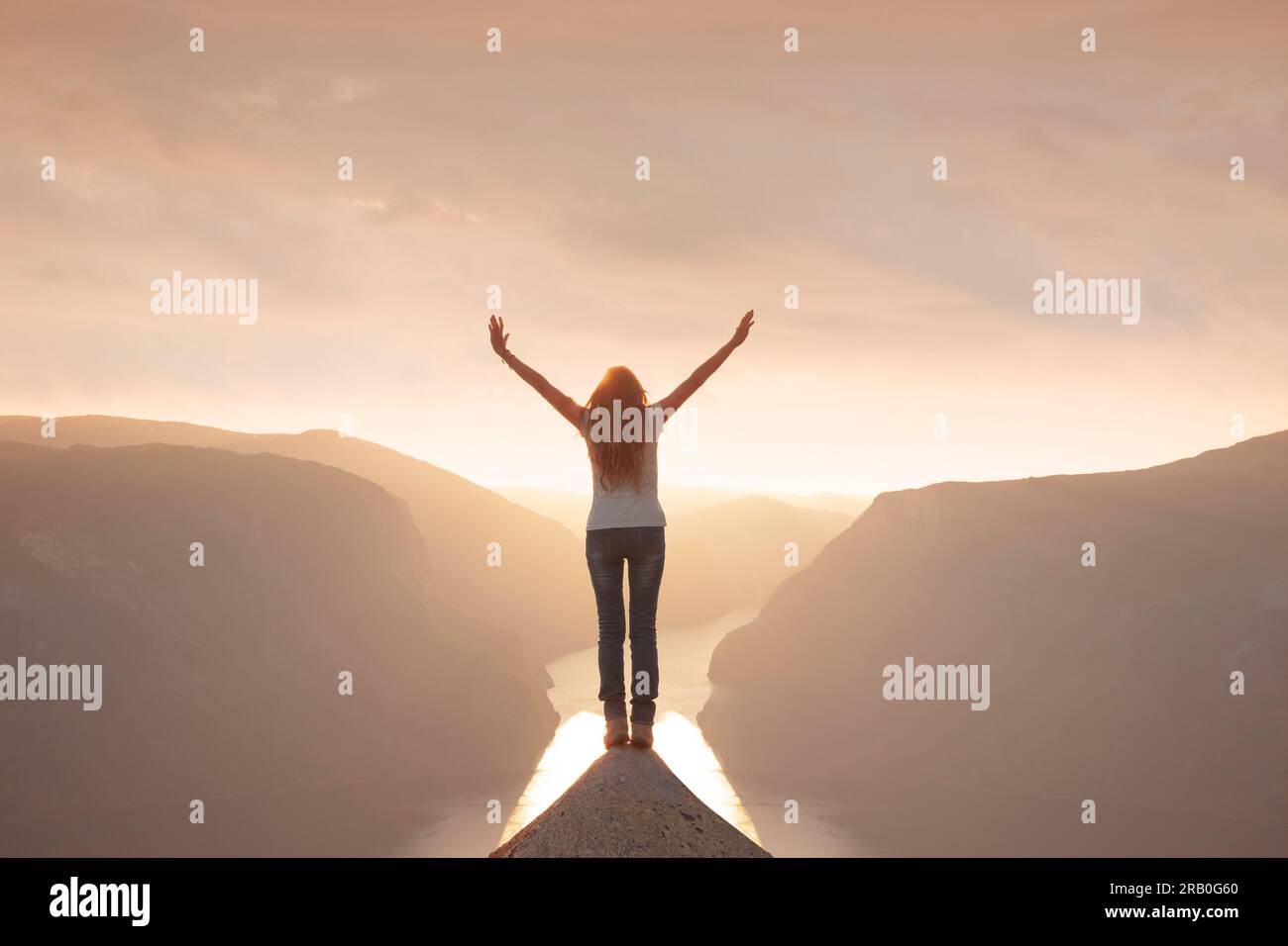 A woman stands silhouetted on a mountain top with arms outstretched Stock Photo