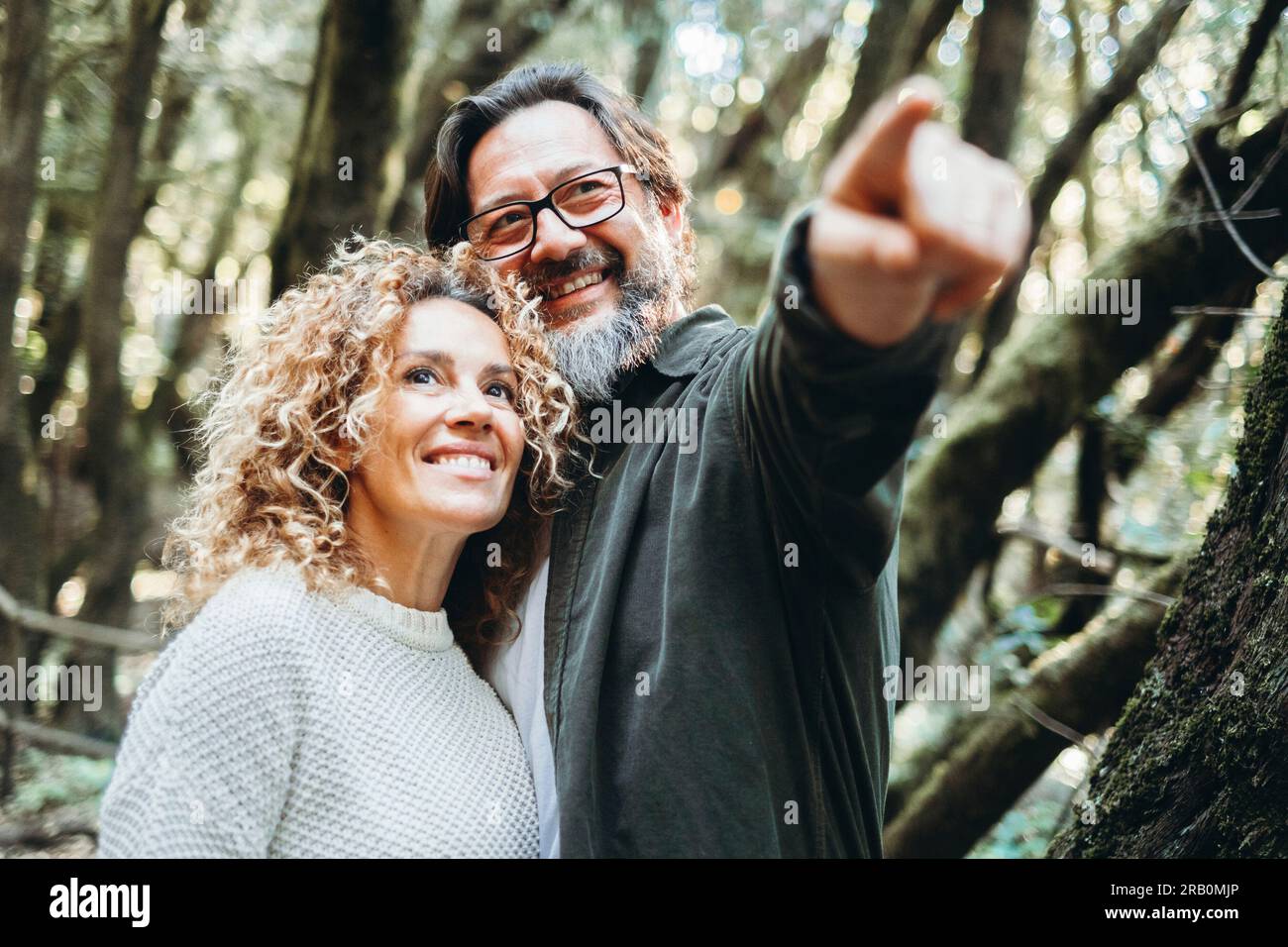 Happy couple of tourist admiring outdoor scenic place in nature forest with green trees and good environment concept. People enjoy together alternative weekend vacation and travel activity outdoors Stock Photo