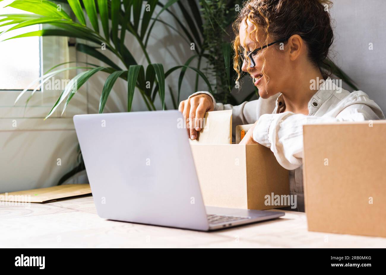 Happy young entrepreneur female preparing package and shipment for express courier after sold article on line in modern start-up home business job lifestyle. New work adventure. Busy woman indoor Stock Photo