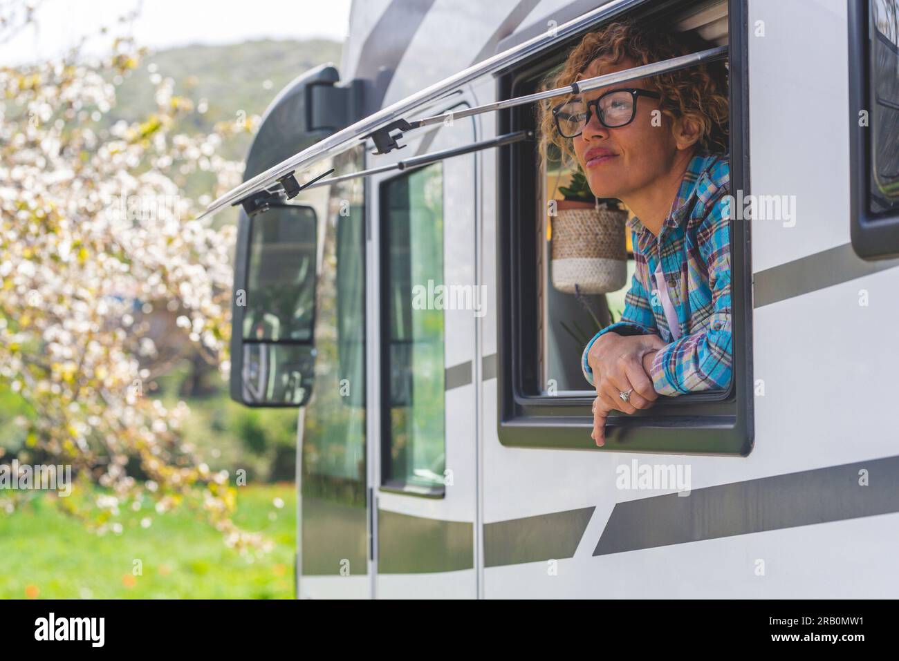 Travel vacation camper van lifestyle. One happy and free alone woman having relax looking outside the window of her modern camper van motorhome. Journey adventure holiday trip. Nature and free parking Stock Photo
