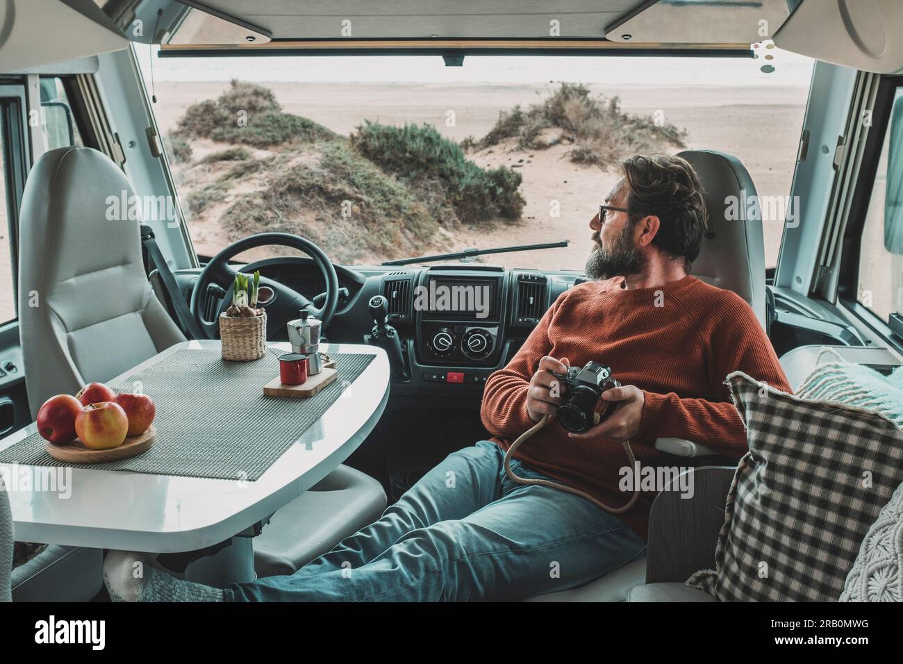 Travel lifestyle and vanlife. Tourist enjoy and relax on vacation sitting inside motorhome vehicle and using photo camera. Traveler photographer. People and adventure. Parking at the beach. Camper van Stock Photo