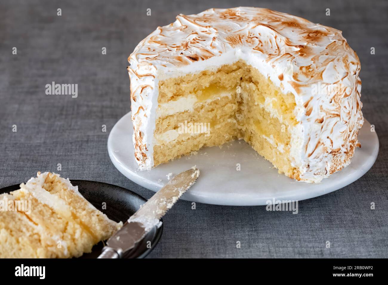 A home made lemon meringue cake served to a table plated. The cake has a lemon curd filling and buttercream frosting and a torched meringue frosting Stock Photo