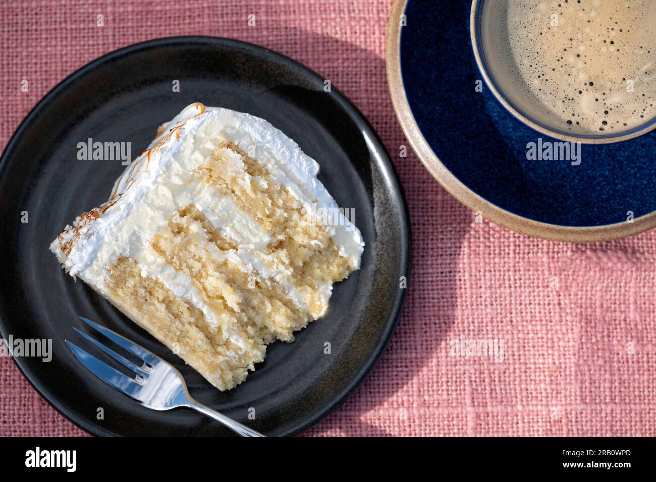 A single plated serving of a home made lemon meringue cake served to a table plated. the cake has a lemon curd filling and buttercream frosting Stock Photo