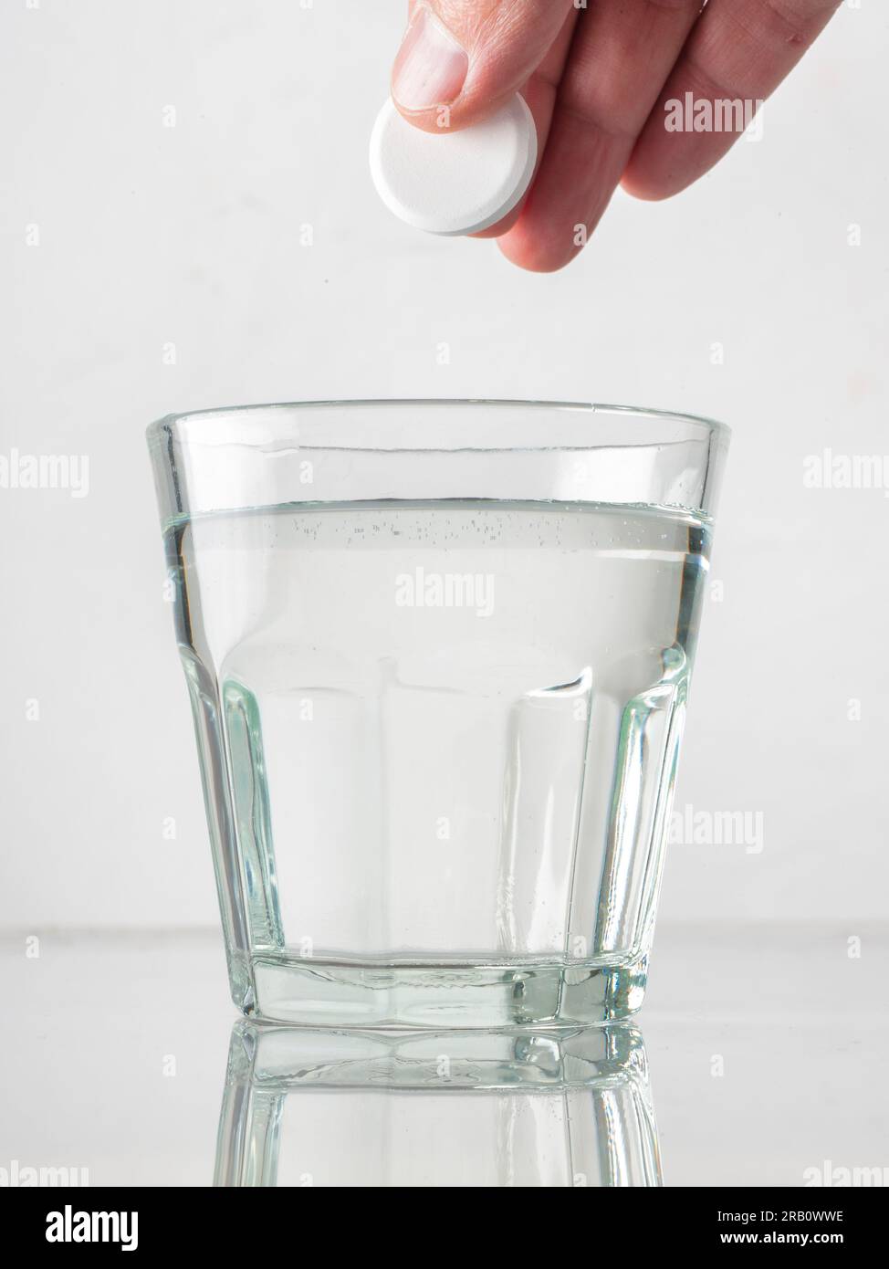 Male hand dropping a painkiller pill in a glass of water Stock Photo