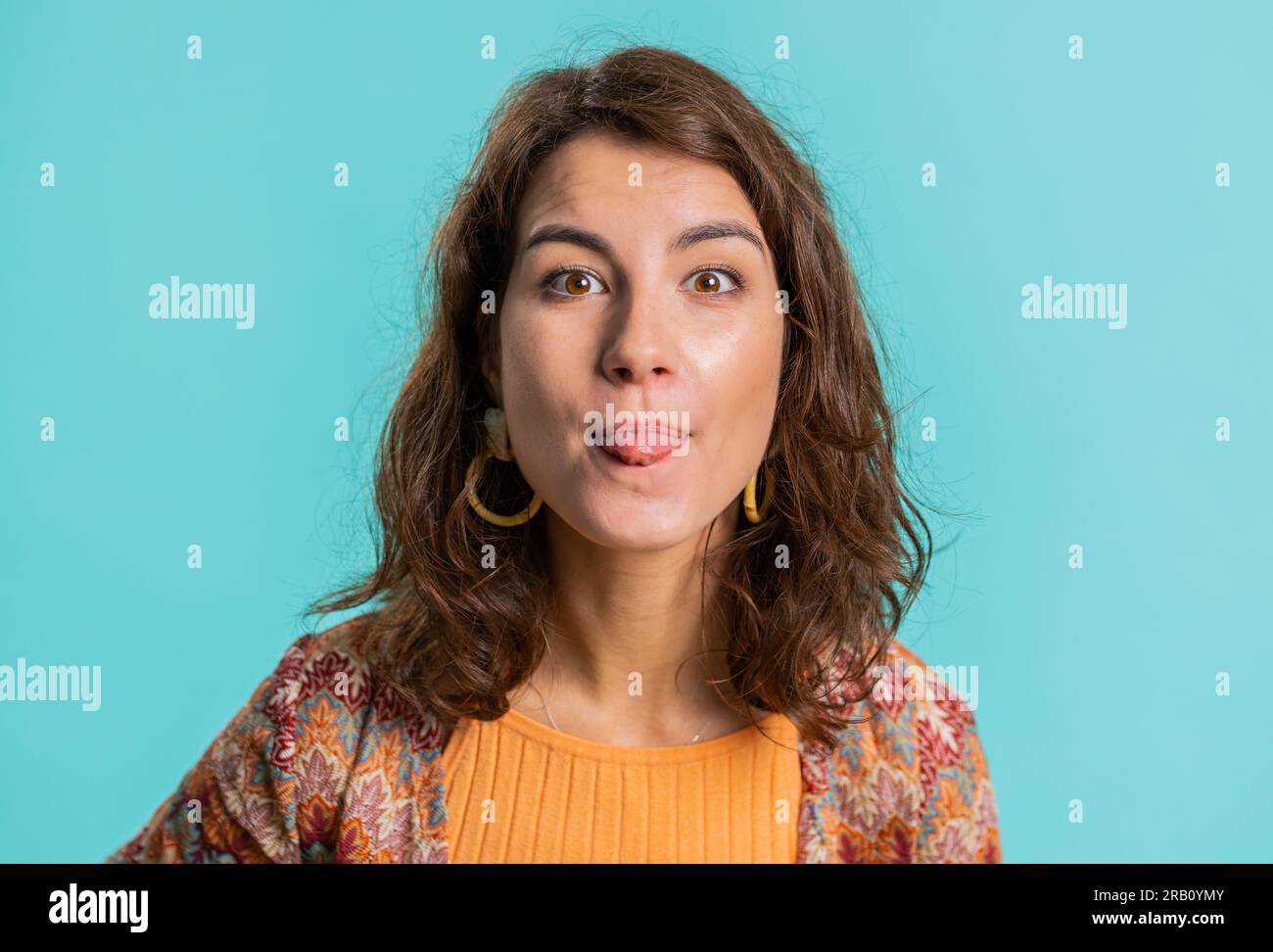 Cheerful funny young woman showing tongue making faces at camera, fooling around, joking, aping with silly face, teasing, bullying, abuse. Girl isolated alone on blue studio background. Lifestyles Stock Photo