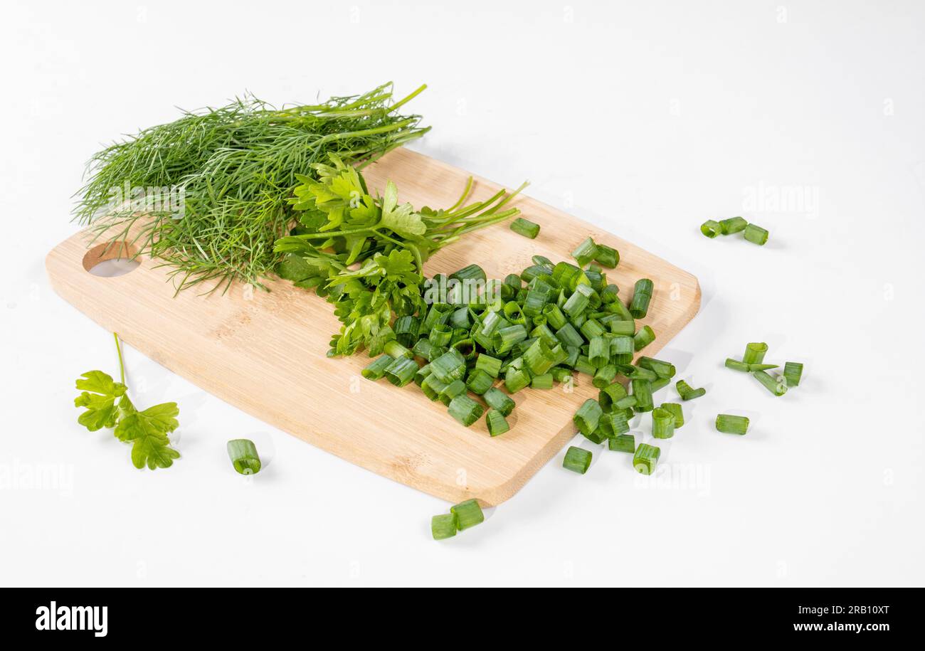 Kitchen board with chopped green onions, parsley and dill. White background Stock Photo