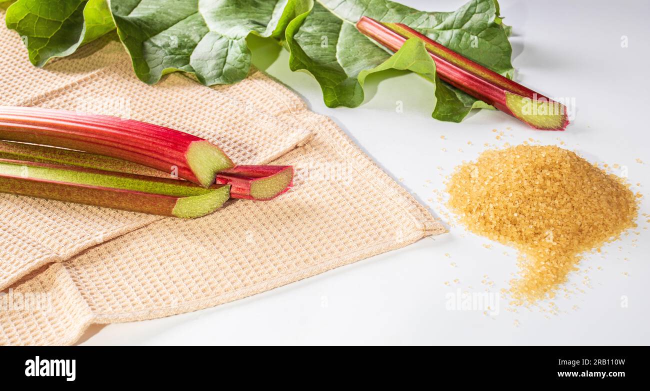 Healthy food. Rhubarb stalks on a waffle towel background, rhubarb leaf and a bunch of brown sugar on a white background Stock Photo
