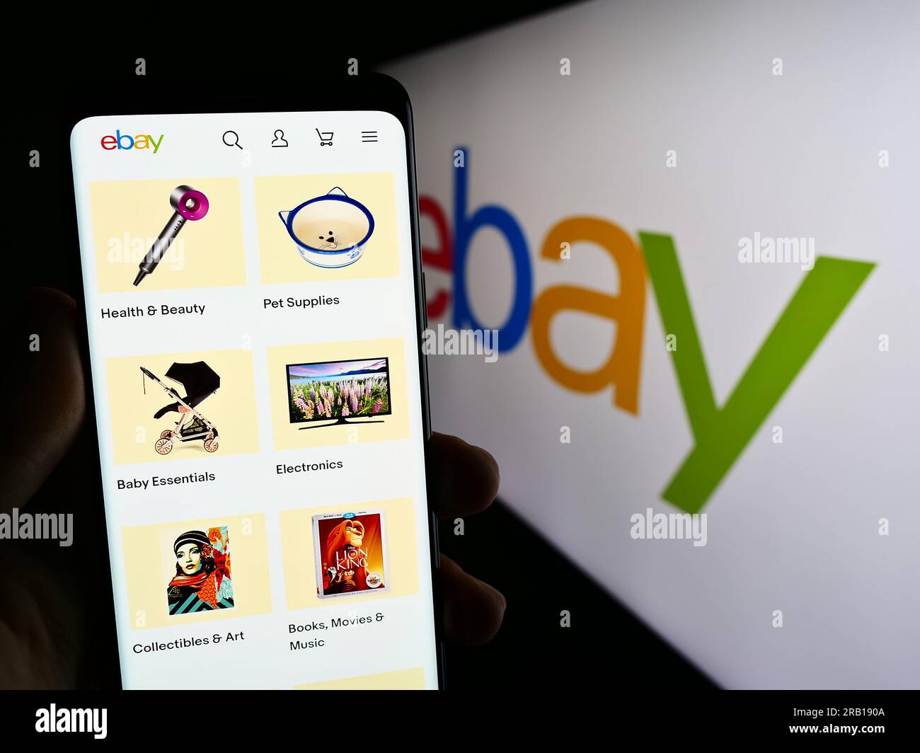 Person holding smartphone with web page of US e-commerce company eBay Inc. on screen in front of business logo. Focus on center of phone display. Stock Photo