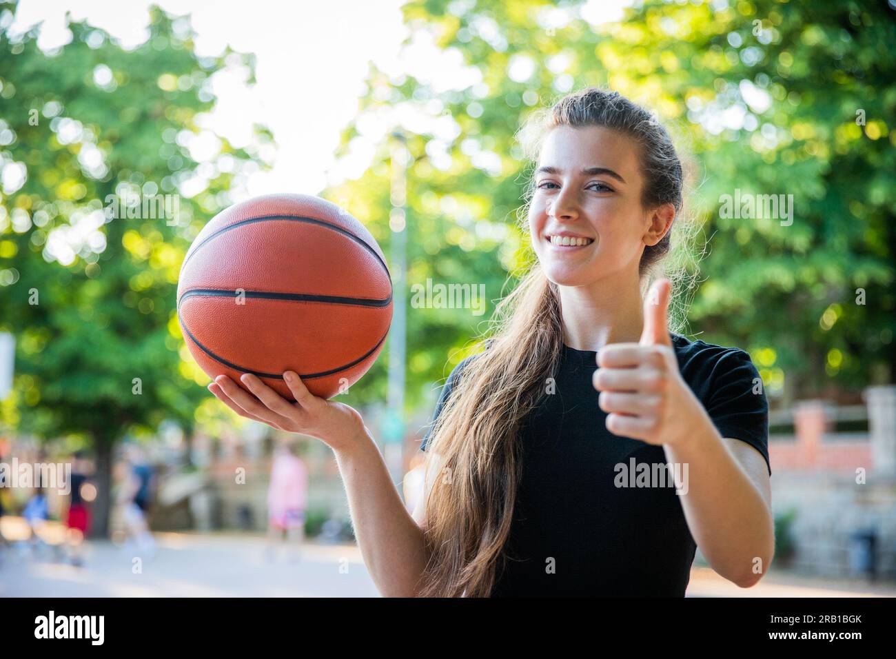 A basketball player with a basketball in her hand shows the thumbs up smiling Stock Photo