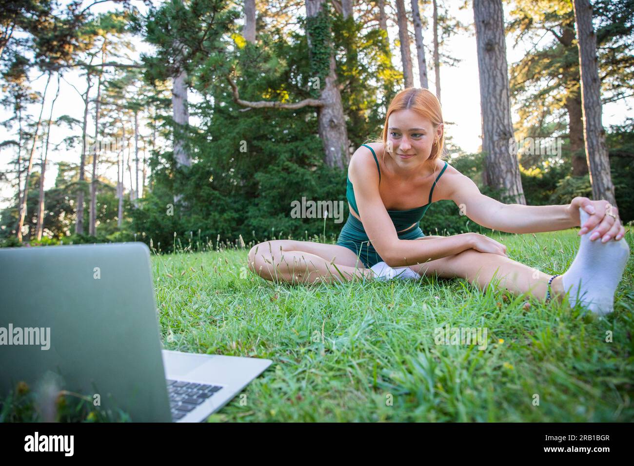 An athlete performs stretching exercises following online lessons with her laptop Stock Photo