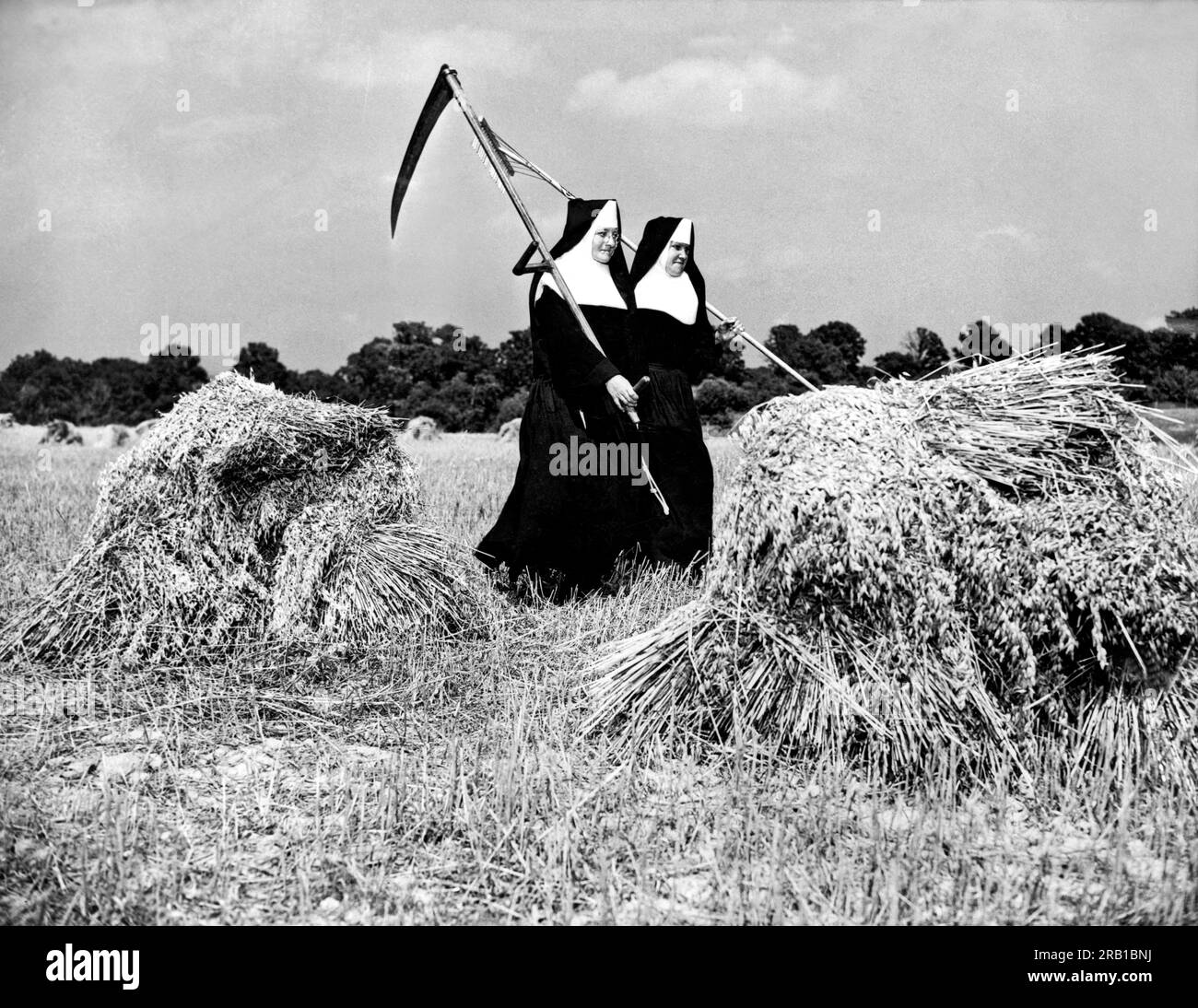 Lemont, Illinois:  August 4, 1942. Two of the nuns at at the Mount Asissi Convent head across the oat fields of the 100 acre farm with scythe and rake to do the harvesting. Stock Photo