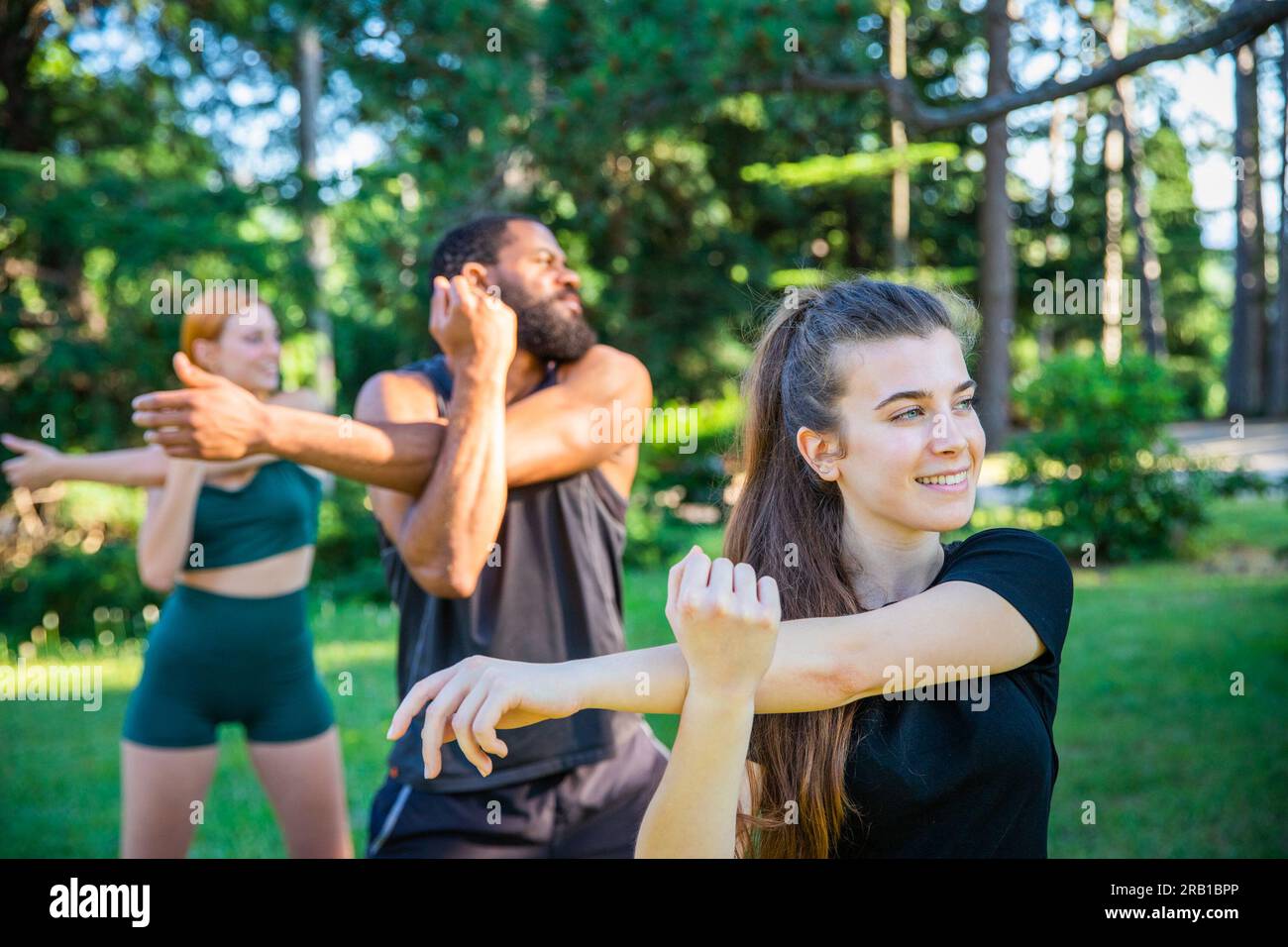 Three athletes train and perform an arm stretch exercise outdoors in a