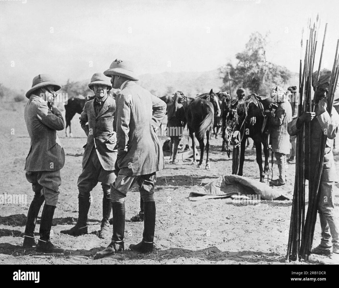 Jodhpur, India:   January 5, 1922 The Prince of Wales fastens his helmet as he chats with Sir Lionel  Halsey and Col. Wogan just before the start of the boar hunt. Mounted beaters drive the boar towards the mounted hunters who then stick the boars with the steel tipped bamboo lances being held by the native at the right. Stock Photo