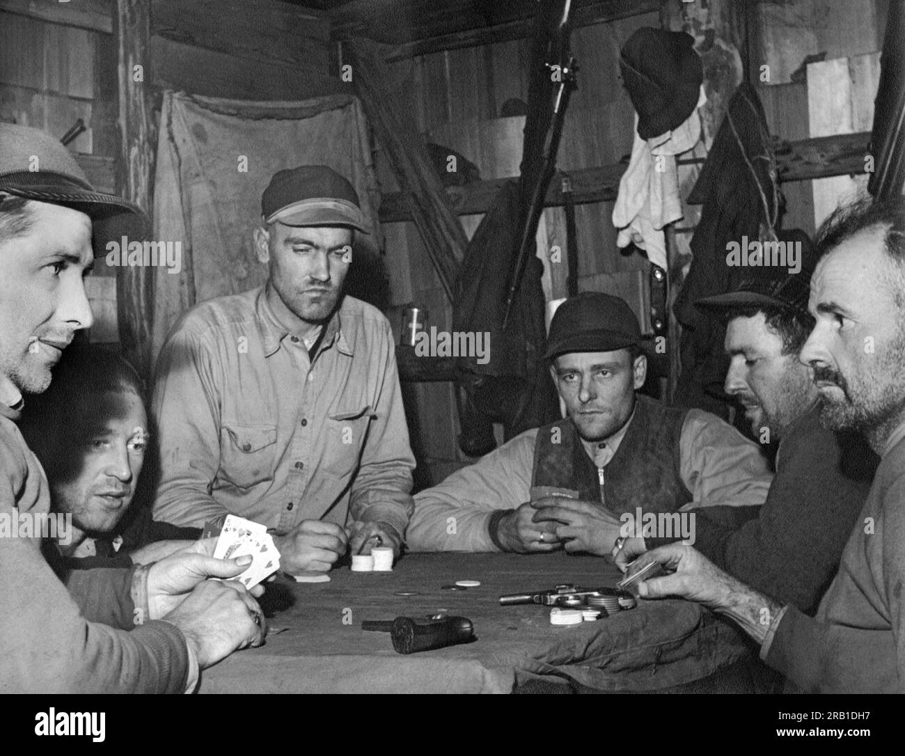 United States:  c. 1935. Six serious looking elk hunters playing poker at a table with two pistols on it. Stock Photo