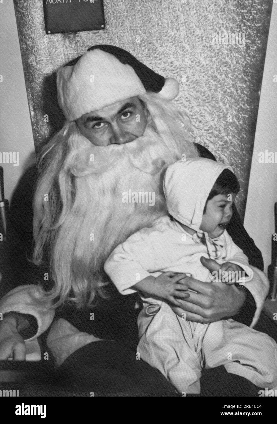 United States:   1951 A frustrated Santa Claus holding an unhappy and crying toddler on his lap. Stock Photo