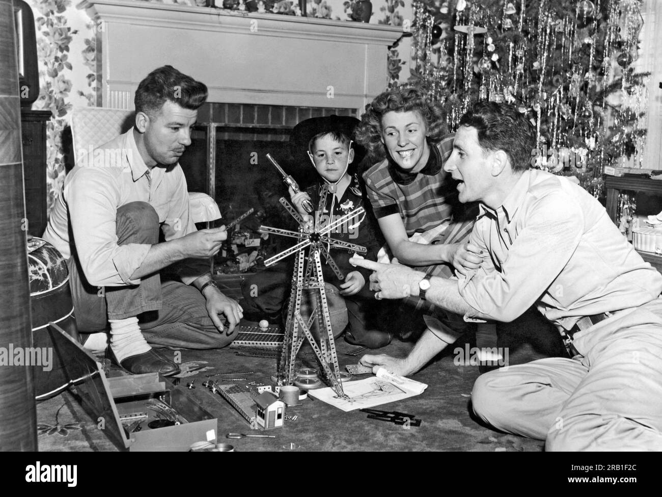 Millbrae, California:  c. 1954. A small boy dressed in a cowboy outfit watches as his parents and friend play with the erector set that he got for Christmas Stock Photo