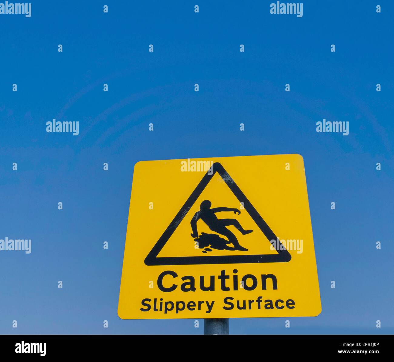 Signage for a slippery surface, a yellow sign set agains a clear blue sky. Stock Photo