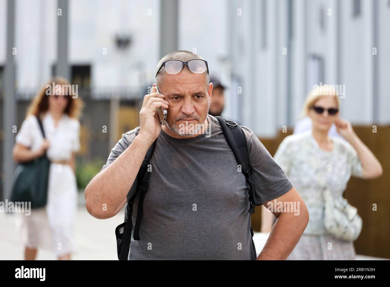 Worried man talking on mobile phone walking down city street on people ...