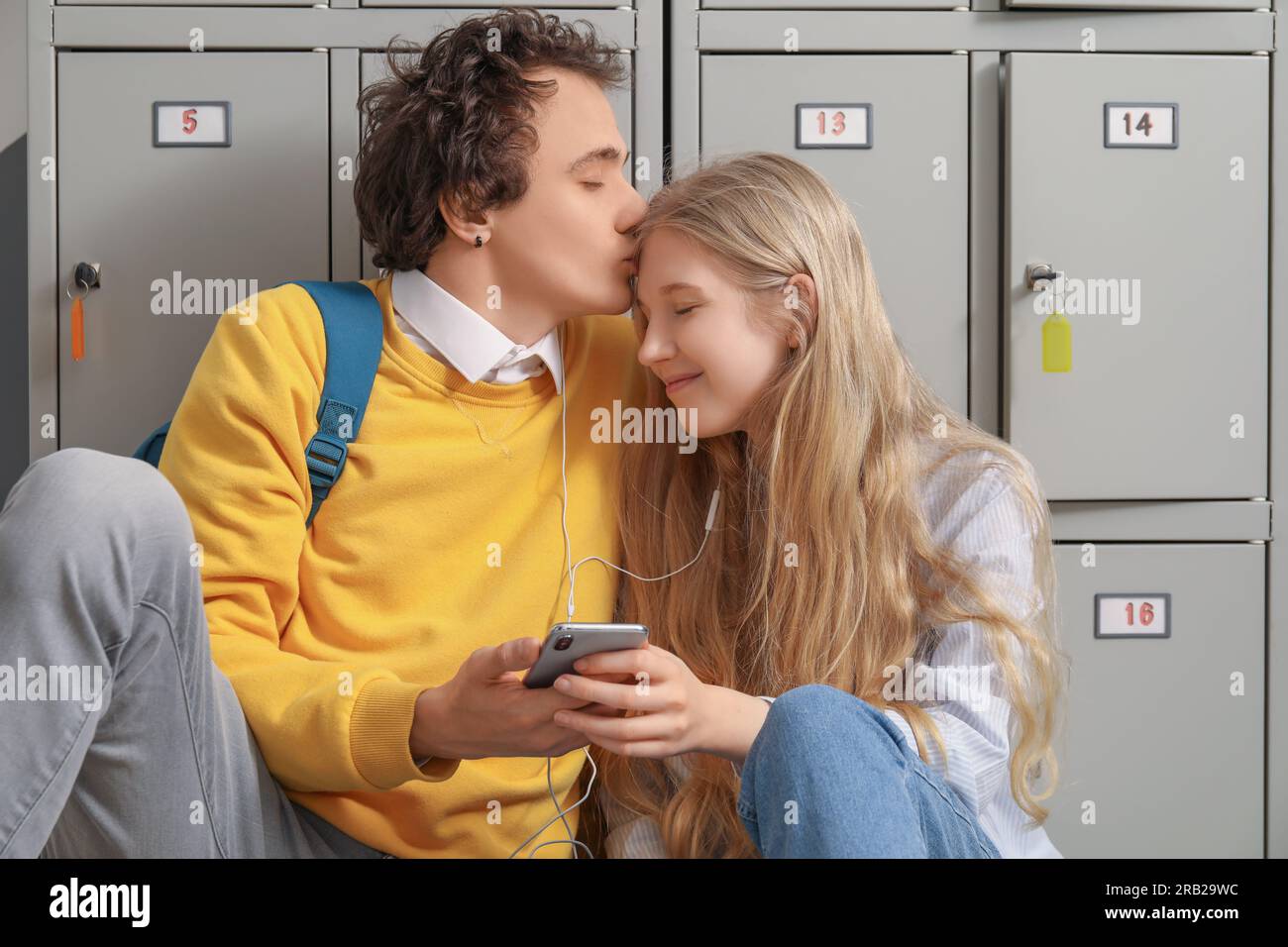 Cute teenage couple with earphones listening to music near locker at school Stock Photo
