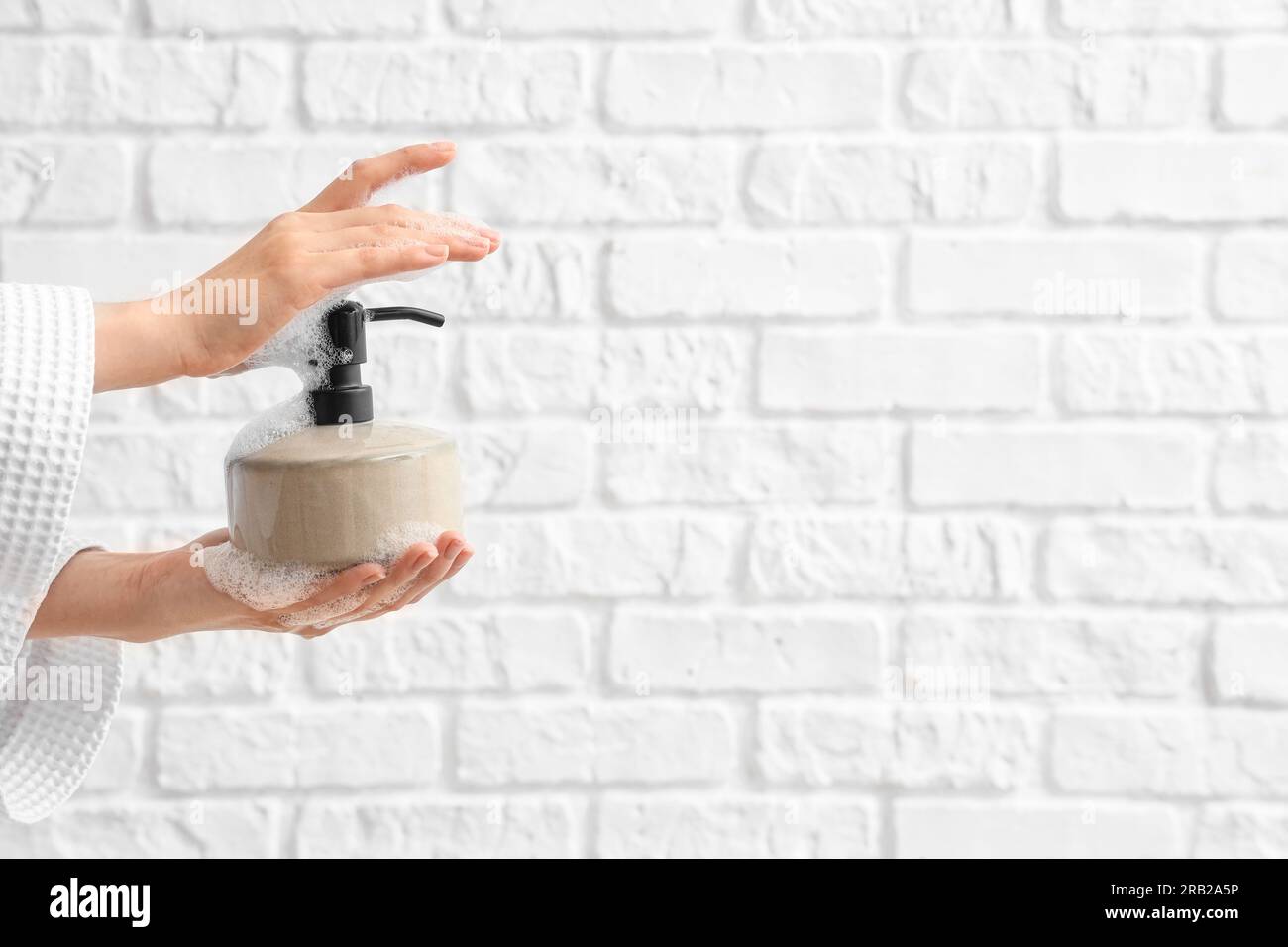 Hands with liquid soap on white brick background Stock Photo
