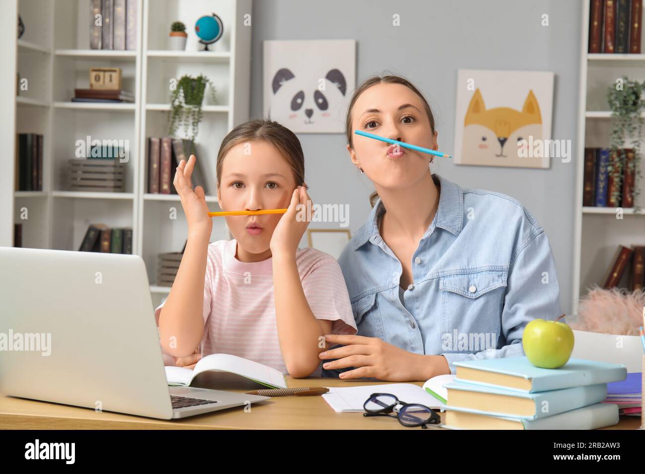 Cute little girl with her mother having fun while doing lessons at home ...