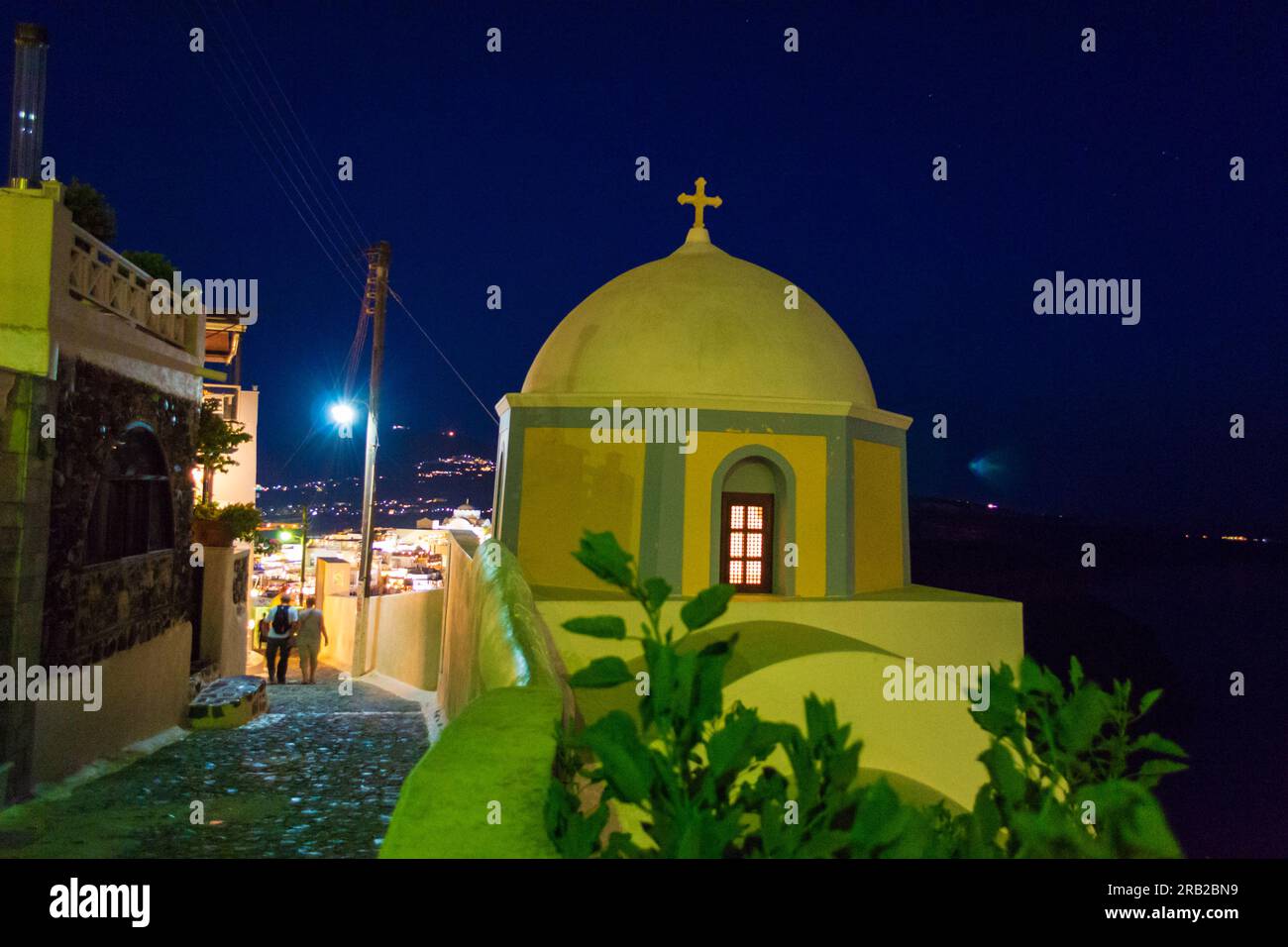 Night view of typical narrow paved street with Catholic Church of Saint Stylianos in Fira on Santorini island clifftop,Greece. Stock Photo