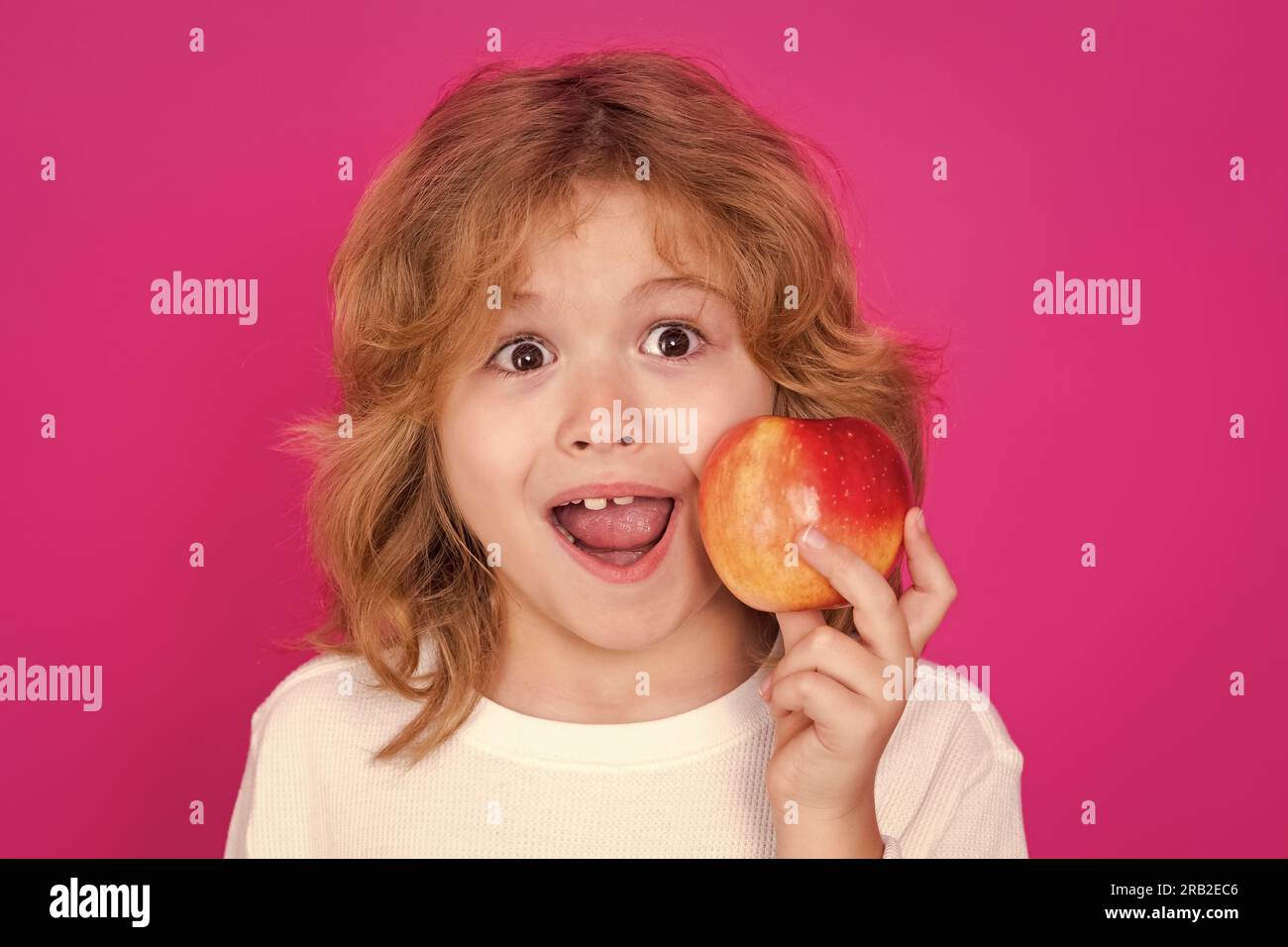 Kids face with fruits. Kid with apple in studio. Studio portrait of cute child hold apple isolated on pink background Stock Photo