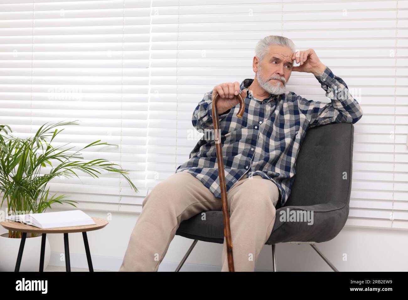 Senior man with walking cane sitting on armchair at home Stock Photo ...