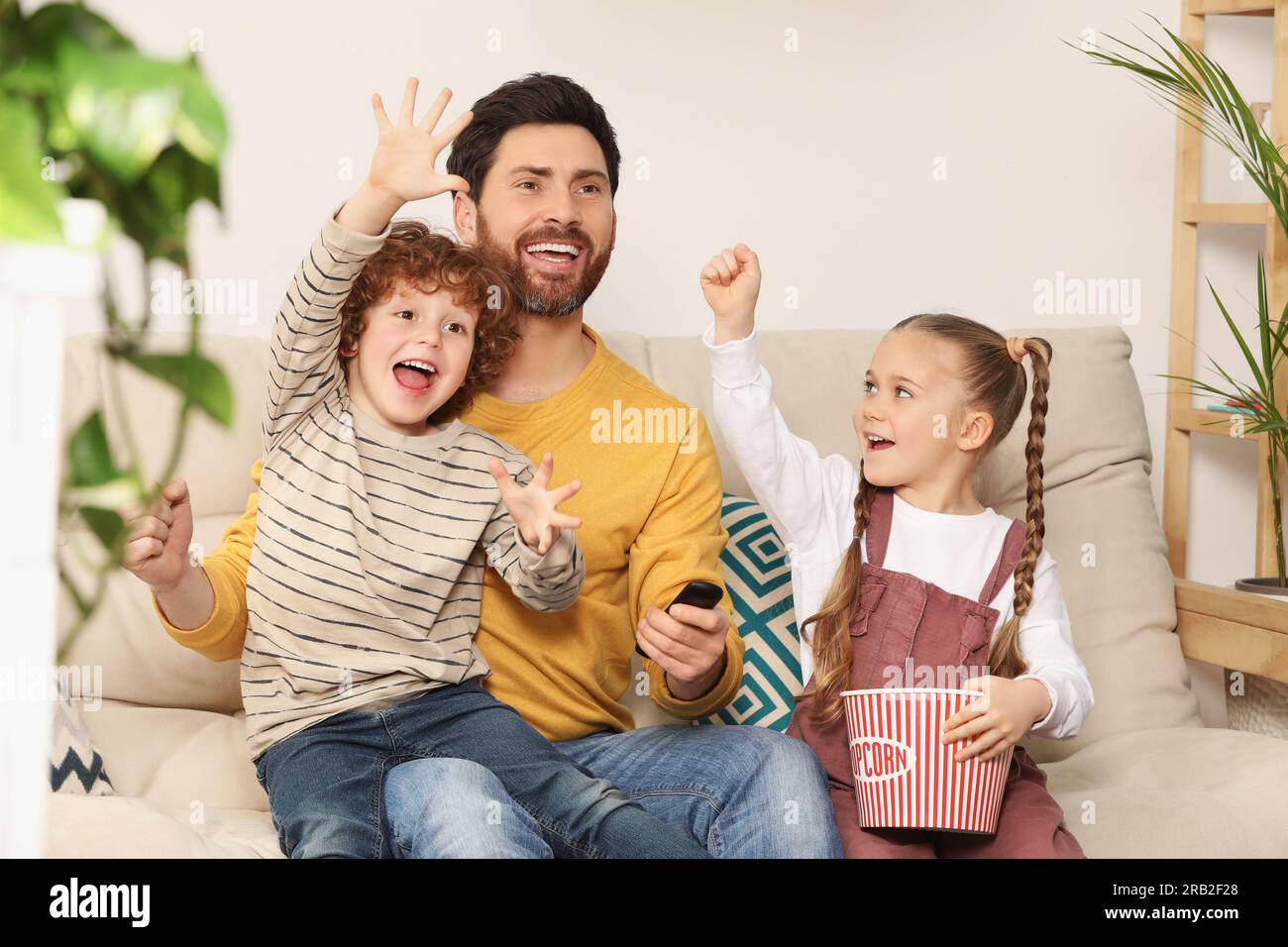 Happy father and children watching TV with popcorn on sofa at home Stock Photo
