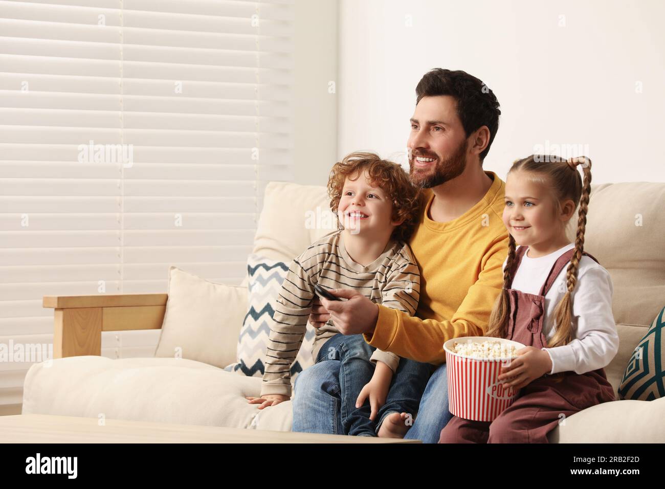Happy father and children watching TV with popcorn on sofa indoors, space for text Stock Photo