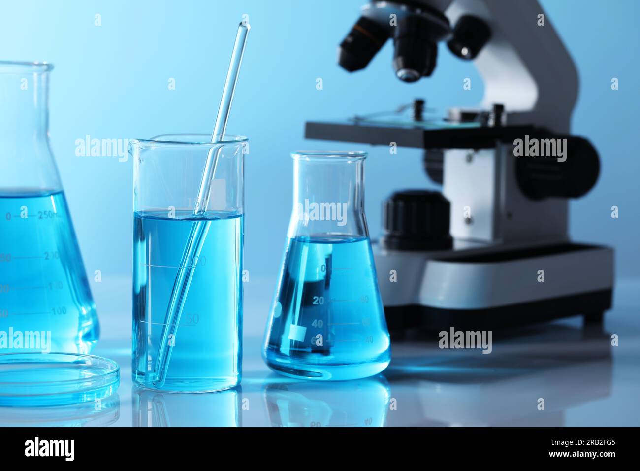 Different laboratory glassware with light blue liquid and microscope on ...