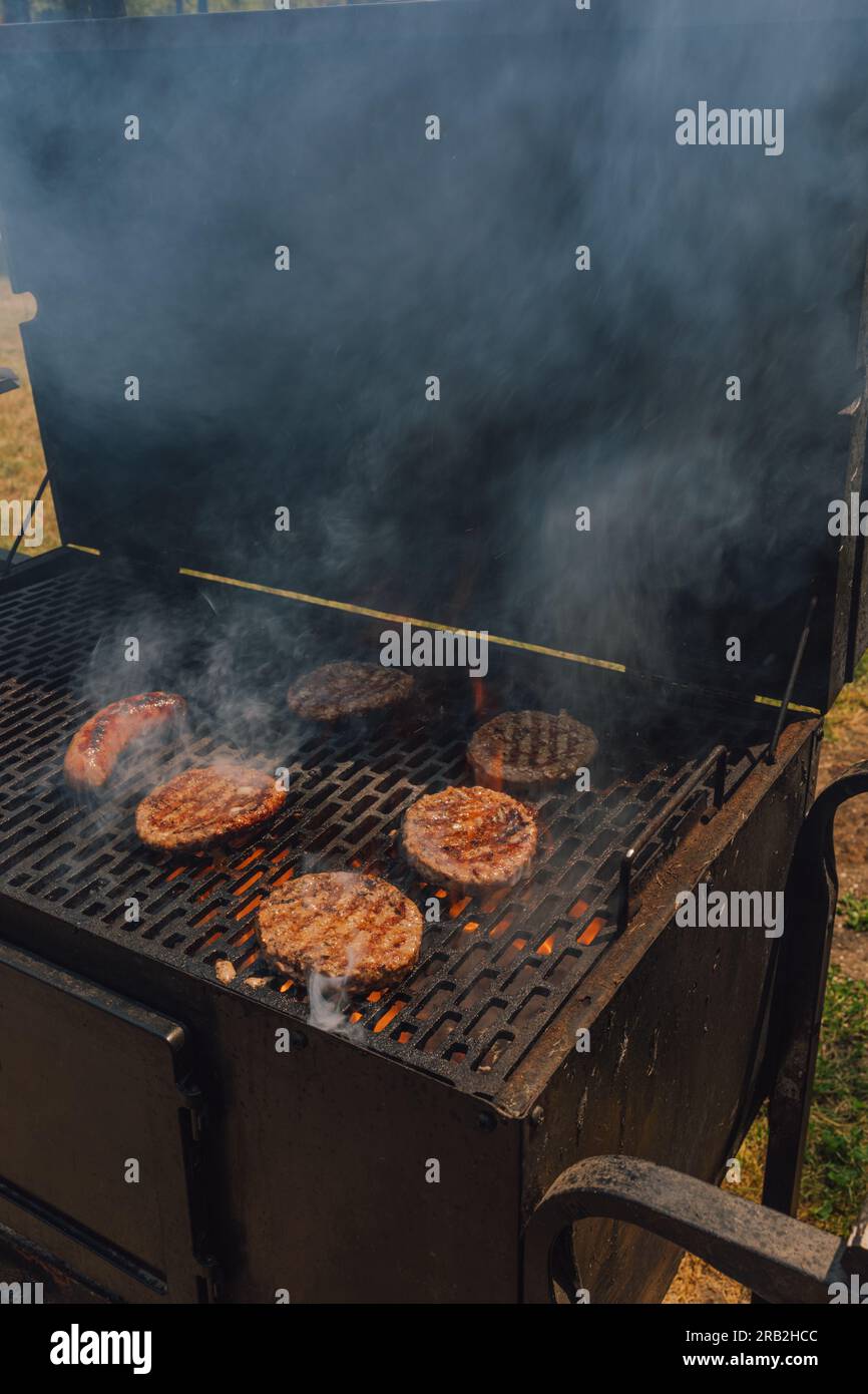 grilling beef burger patties on charcoal barbecue outdoors, smoky Stock