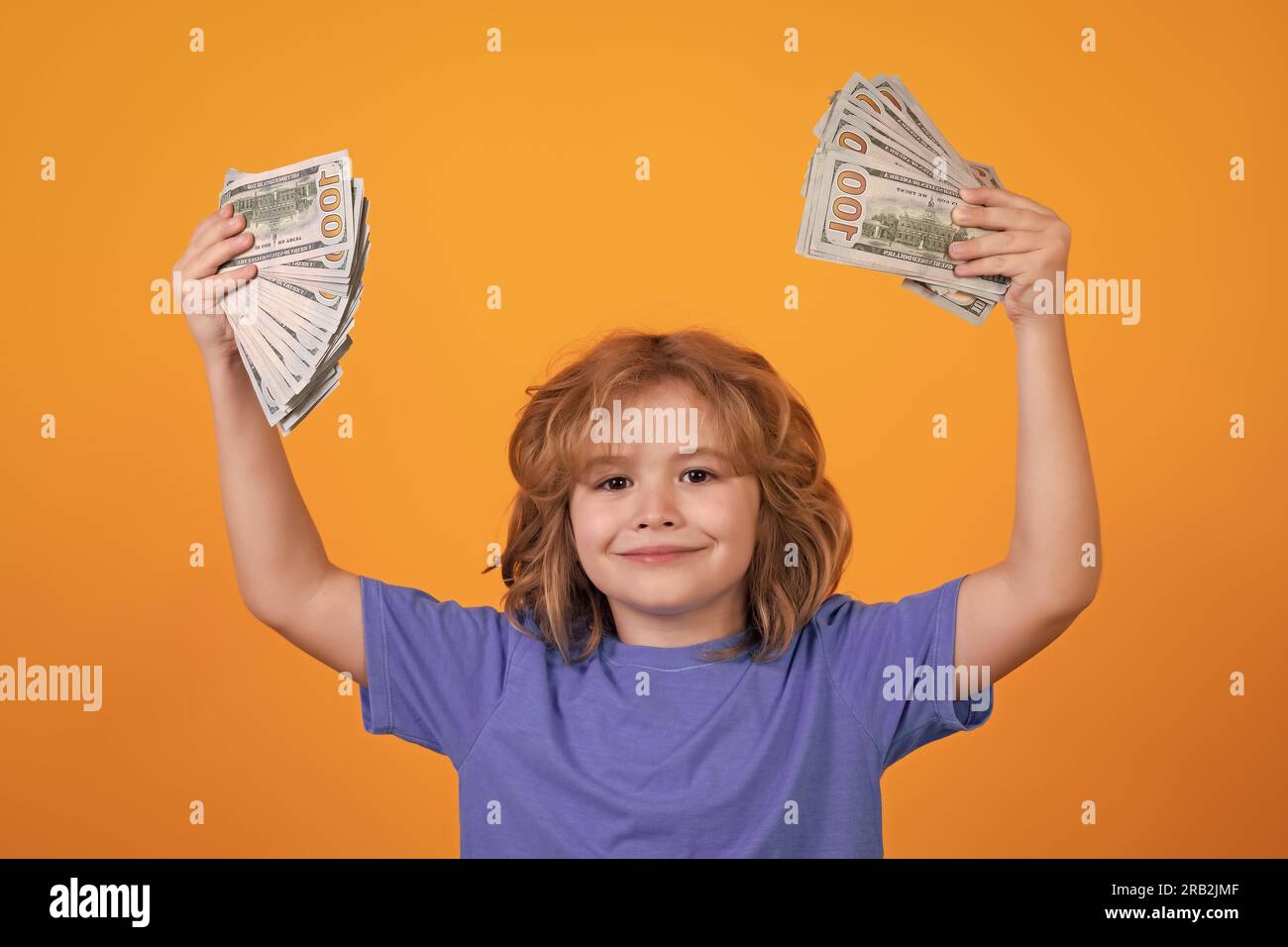 Kid showing money dollar bills, standing dreamy of rich against isolated yellow studio background Stock Photo