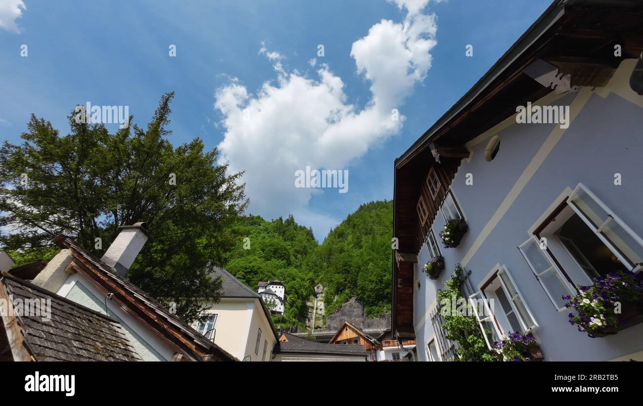 Street life in Hallstatt; building, mountain, blue sky clouds, trees Stock Photo