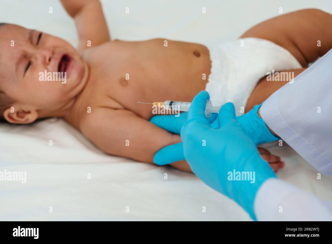 doctor holding syringe and preparing vaccine giving injection to arm of crying infant baby Stock Photo