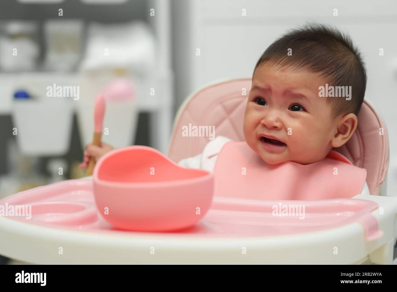 crying infant baby eating food with a spoon at home Stock Photo