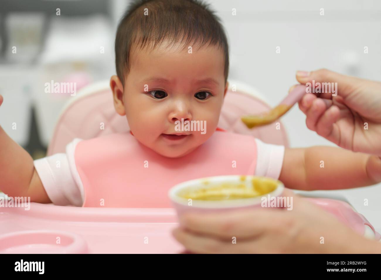 mother feeding food to her infant baby with a spoon at home Stock Photo