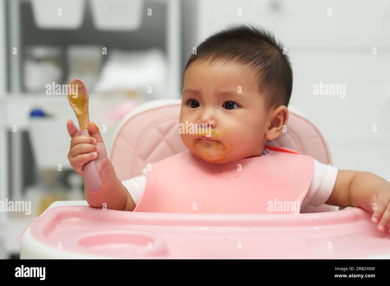 happy infant baby eating food itself with a spoon at home Stock Photo