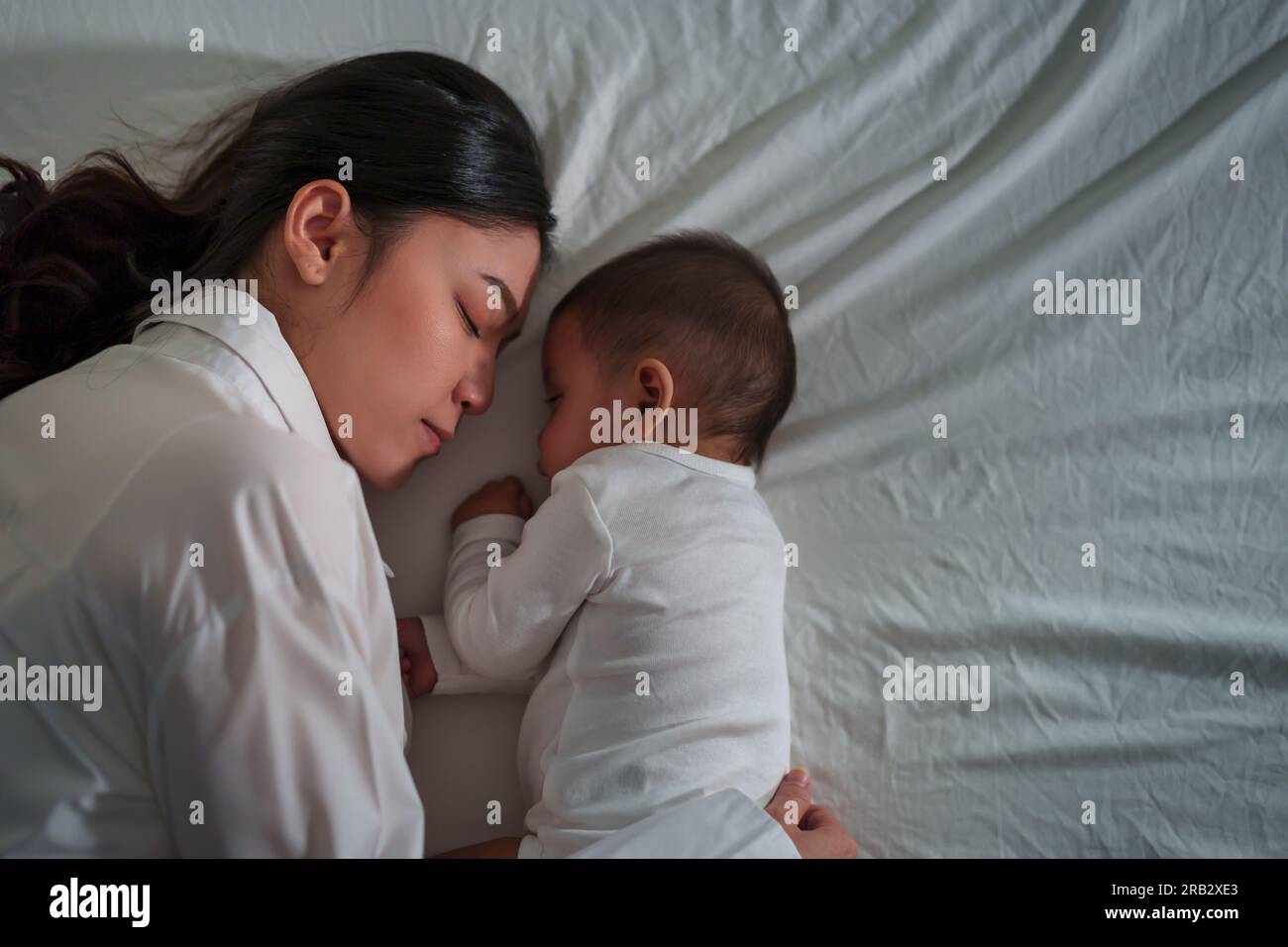 mother embraces the infant baby sleeping together in a bed at night Stock Photo
